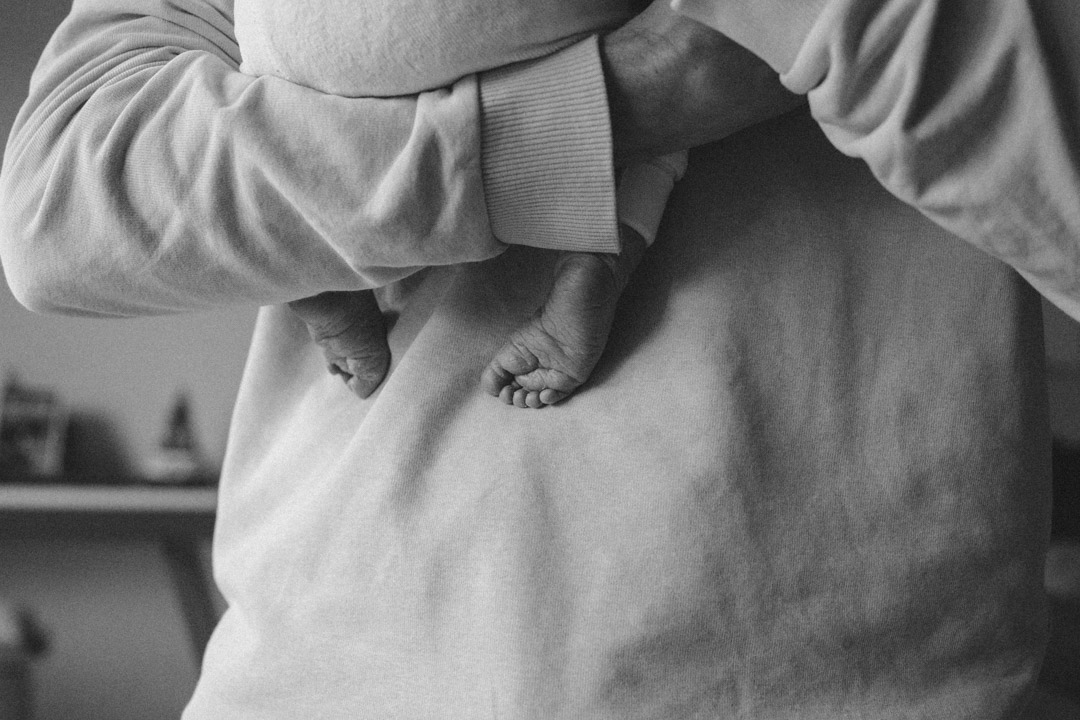 Ein Vater hält sein neugeborenes Baby auf dem Arm. Es sind nur die kleinen Füße zu sehen. Festgehalten in schwarzweiß.