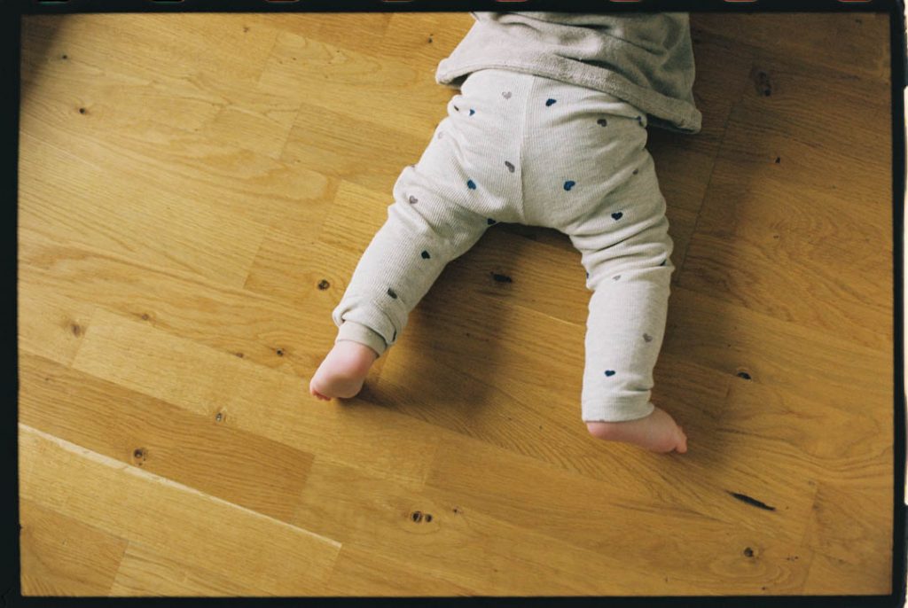 Krabbelndes Baby auf Parkett. So sehen sind nur die Beine.