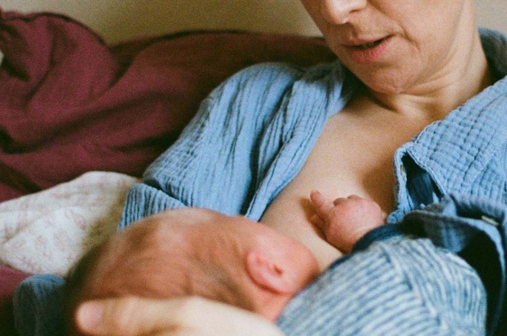 Mutter im Wochenbett stillt ihr Neugeborenes. Die Hand des Säuglingsliegt auf der Brust der Mutter.