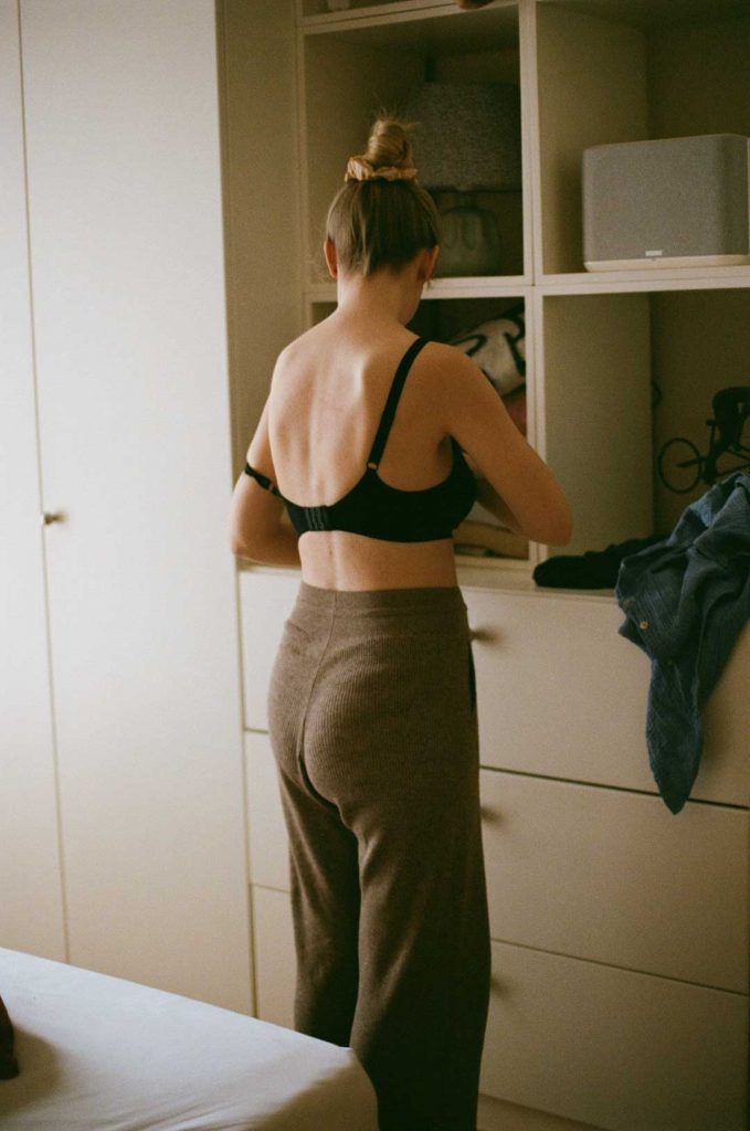 Mutter im Wochenbett bereitet sich für das Stillen ihres Babys vor. Sie ist von hinten in ihrem Schlafzimmer zu sehen. Ihr Rücken ist frei.