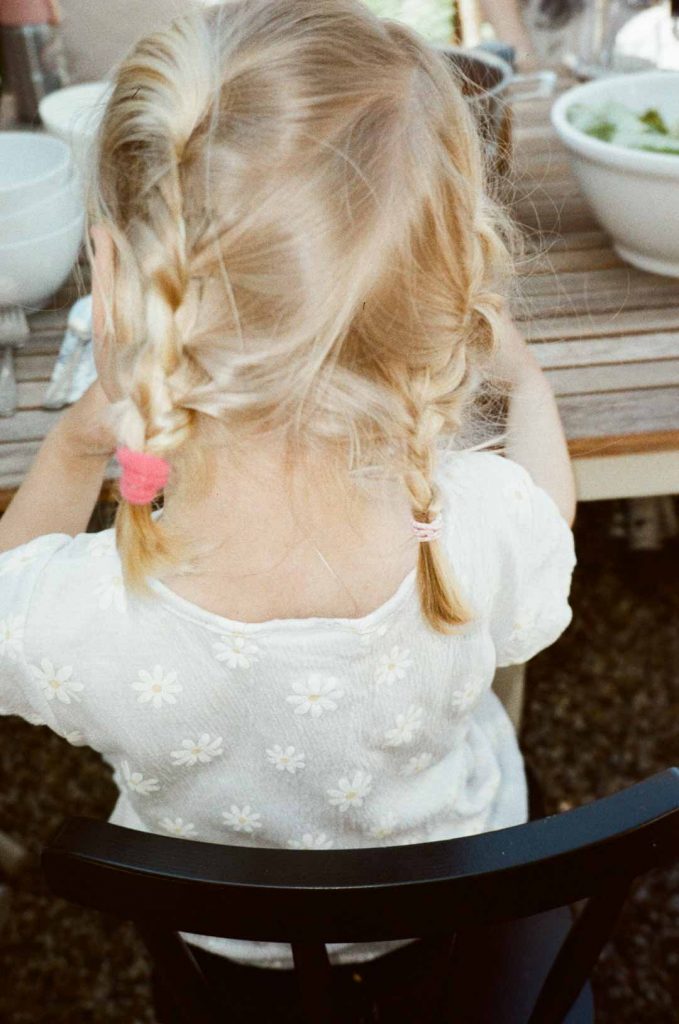 Kleines blondes Mädchen mit geflochtenen Zöpfen, dass von hinten aufgenommen wurde.