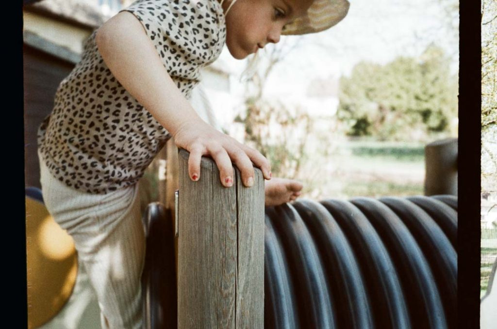 Kleines Mädchen klettert konzentriert auf dem Spielgerüst eines Spielplatzes.