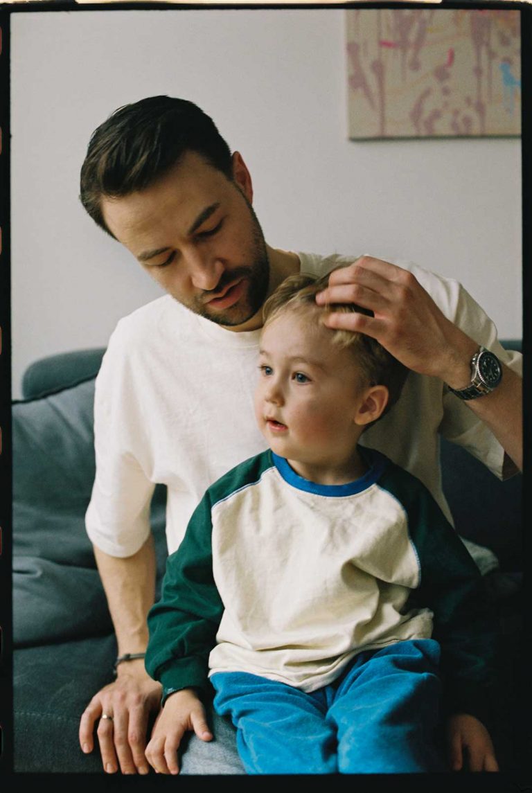 Ein kleiner Junge auf dem Schoß seines Vaters. Er streicht ihm liebevoll die Haare aus dem Gesicht.