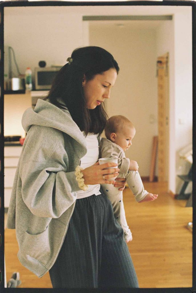 Mutter trägt ihr Baby durch die Küche. In der anderen Hand hält sie eine Kaffeetasse